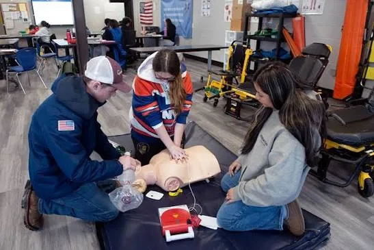 A CPR class practicing compressions on a training manikin with an AED